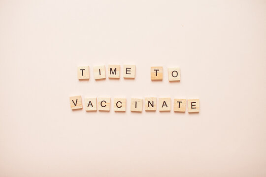 Phrase time to vaccinate made from wooden blocks on a light pink background. High quality photo