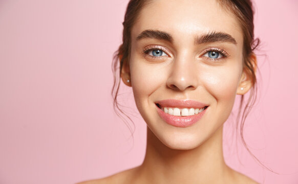 Portrait Of Caucasian Young Woman With Blue Eyes And Perfect White Smile, Nude Lips Gloss And No Makeup Natural Look, Gazing Happy At Camera With Clean Hydrated Facial Skin, Pink Background