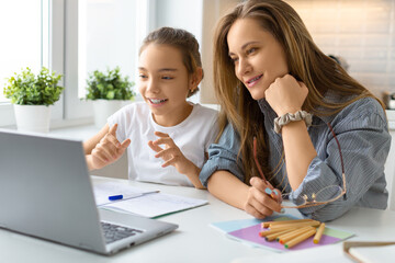 Obraz premium Smiling mom and daughter in front of a laptop monitor.
