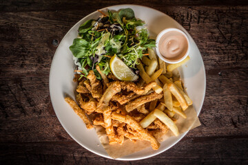 Crispy Calamari fried with cocktail sauce lemon and salad on a wooden table
