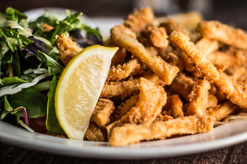 Crispy Calamari fried with cocktail sauce lemon and salad on a wooden table
