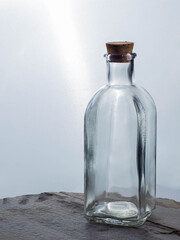 Empty glass bottle with cork stopper, on white background, on wooden base.