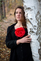 woman in black dress with red flower standing in forest looking sad