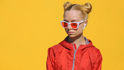 Portrait of happy teenager blonde girl in headphones sunglasses listens to music on smartphone,...