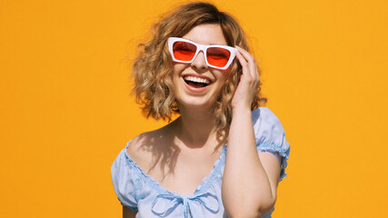 Portrait of happy pretty woman stylish white sunglasses with red glasses raises up, smiling with pleasure on yellow background in summer. Emotions. Positive girl. Lifestyle. Freedom