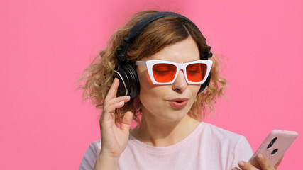 Portrait happy woman in headphones, stylish sunglasses listens to music on smartphone sings,...
