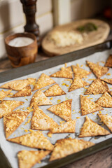 Process of cooking cheese Tortilla chips with olive oil on baking sheet before oven, homemade salty savory pastry snack in the kitchen. Selective focus with copy space.