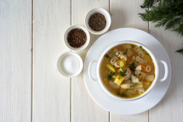 Hearty lunch: chicken soup with pasta and potatoes in a white plate on a white table