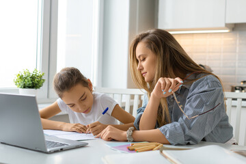 Fototapeta premium Mom helps her daughter during online meet with teacher. Family support concept.