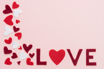 Composition for Valentine's Day February 14th. Soft delicate pink background red hearts cut out of felt and word love.  Greeting card. Flat lay top view copy space 2021 Lo.ve cute concept frame.