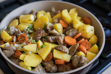 Meat stewed with potatoes, carrots, vegetables and spices in a pan. Process of cooking dish in a kitchen. Selective focus with copy space