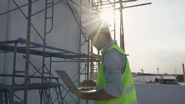 The engineer using a computer laptop and went to inspect the site's construction, and there was a steel scaffold in the back.