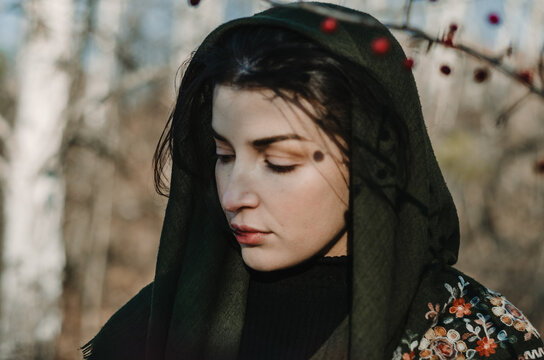 Side Portrait Of A Woman With A Green Forest Scarf Over Head With Neutral Expression Looking Down, With Shadows Over Face