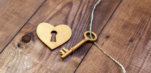 Top view shot of gold heart and key on wood background with copy space