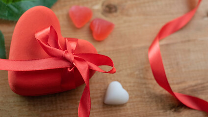 Closed red box in the shape of a heart with a red ribbon bow on wooden background with copy space. Photo of a gift box for Wedding, New Year, Christmas or Valentines Day. Top view. Close-up.