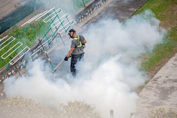Healthcare worker using Fogging machine spraying chemical to eliminate mosquitoes and kill larvae to fight against the spread of dengue fever, Zika virus or Malaria at a residential area.