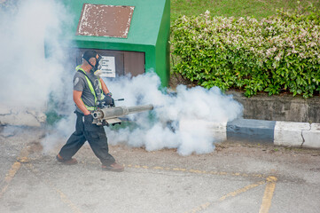 Healthcare worker using Fogging machine spraying chemical to eliminate mosquitoes and kill larvae to fight against the spread of dengue fever, Zika virus or Malaria at a residential area.