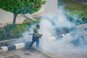 Healthcare worker using Fogging machine spraying chemical to eliminate mosquitoes and kill larvae to fight against the spread of dengue fever, Zika virus or Malaria at a residential area.