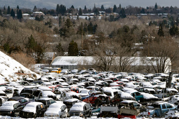 Junkyard full of snow covered cars and trucks.