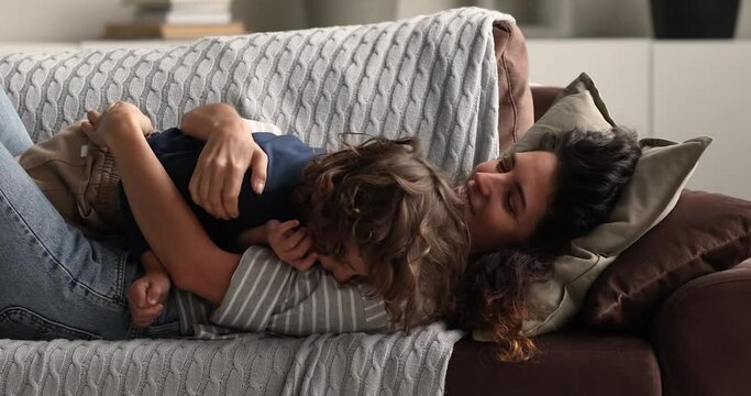 Young loving mother and little adorable son lying on soft comfy couch enjoy free carefree time tickling each other having fun at home. Babysitter playing with kid boy, family bond and playtime concept