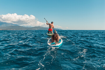 Young happy and beautiful woman sleeping on SUP stand up paddle boards man rowing on a hot day in the Adriatic sea in Montenegro