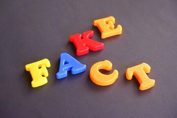 Fake and fact words in colorful plastic magnetic letters on a dark grey black background