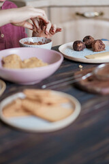 Child hands making sweet balls cookies called Potato of marzipan, biscuits, cocoa. Process of dessert cooking, wooden table with ingredients. Selective focus, copy space