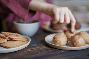 Child hands making sweet balls cookies called Potato of marzipan, biscuits, cocoa. Process of dessert cooking, wooden table with ingredients. Selective focus, copy space