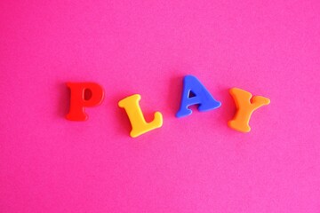 Play word in colorful plastic magnetic letters on a pink purple background