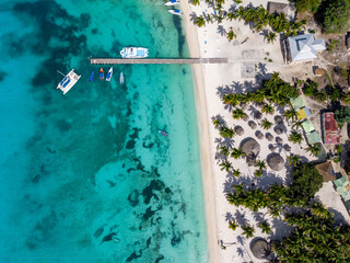 Aerial drone view of the paradise beach with pier, boats, yacht, palm trees and blue water of Caribbean Sea, Saona island, Dominican Republic