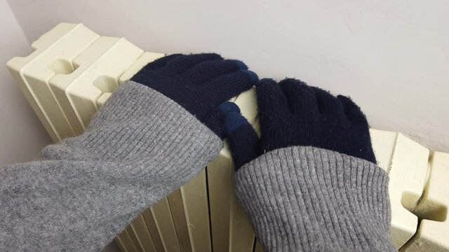 Frozen person with knitted gloves warms up near a radiator