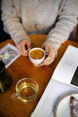a woman in a warm light sweater holds a cup of coffee with her hands