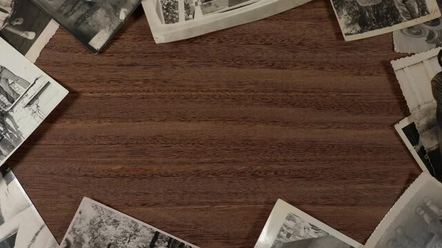 Top view flatlay 4k stock video footage of brown wooden background and collection of old vintage black and white photographs with copy space in middle of frame