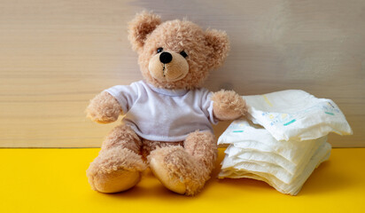 Baby diapers and teddy on yellow color floor - obrazy, fototapety, plakaty