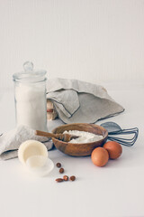Homemade baking ingredients and accessories. A jar of sugar, a cup of flour, eggs, a whisk, a cake pan, a napkin, nuts on a white table. Home hobbies authentic cooking concept, close-up, copy space