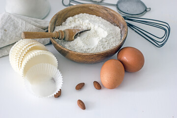 Homemade baking ingredients and accessories. A jar of sugar, a cup of flour, eggs, a whisk, a cake pan, a napkin, nuts on a white table. Home hobbies authentic cooking concept, close-up, copy space