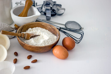 Homemade baking ingredients and accessories. A jar of sugar, a cup of flour, eggs, a whisk, a cake pan, a napkin, nuts on a white table. Home hobbies authentic cooking concept, close-up, copy space