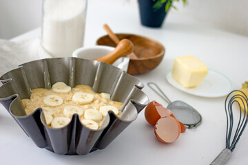 Authentic food banana pie dough in a baking dish surrounded by ingredients on a white table in the...