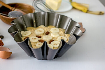 Authentic food banana pie dough in a baking dish surrounded by ingredients on a white table in the kitchen, close-up. Home cooking concept, cooking hobby. The process of making healthy baked goods