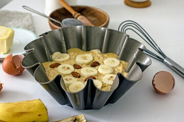 Authentic food banana pie dough in a baking dish surrounded by ingredients on a white table in the...