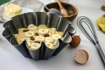 Authentic food banana pie dough in a baking dish surrounded by ingredients on a white table in the kitchen, close-up. Home cooking concept, cooking hobby. The process of making healthy baked goods