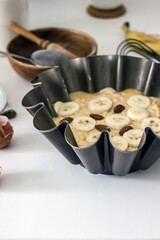 Authentic food banana pie dough in a baking dish surrounded by ingredients on a white table in the kitchen, close-up. Home cooking concept, cooking hobby. The process of making healthy baked goods