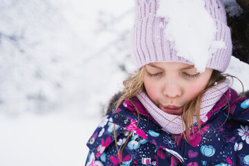 Little sad girl after snowball hit. Kid walking, playing in beautiful winter forest, park among...