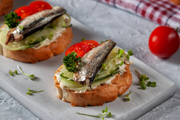 Smoked sprat sandwich - fish, fresh cucumber and tomato. Sprat sandwiches on toasted slices of bread