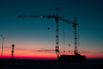 Horizontal outdoors photo with a silhouettes of two construction tower  creanes on the construction...