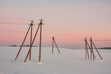 Fototapeta premium Horizontal landscape photo with vintage electricity power line two leg support installed on the snow-covered field at countryside in winter