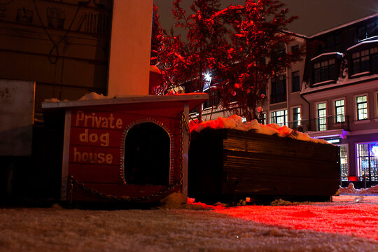 Horizontal conceptual dark photography with a prviate wooden dog house near the corner of a building in city street at winter night