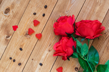 Red roses and candy in the shape of a heart on a wooden background.