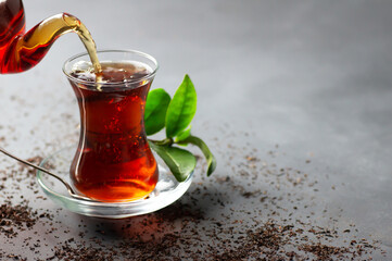 Glass cup of black tea pouring from teapot with fresh tea leaves, traditional turkish brewed hot drink - obrazy, fototapety, plakaty