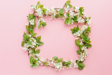 square natural spring frame made of thin twigs of cherry or apple blossom on a pink background, place for text 